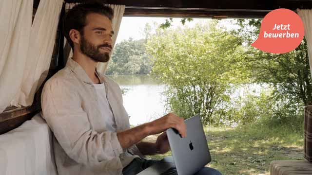 Videoportrait Hannover Junger bärtiger Mann arbeitet mit einem Laptop im Camper mit Blick auf Natur, Bäume und Wasser. Über dem Bild steht „Jetzt bewerben“. Titelbild eines von 52° Film produzierten Recruitingvideos.