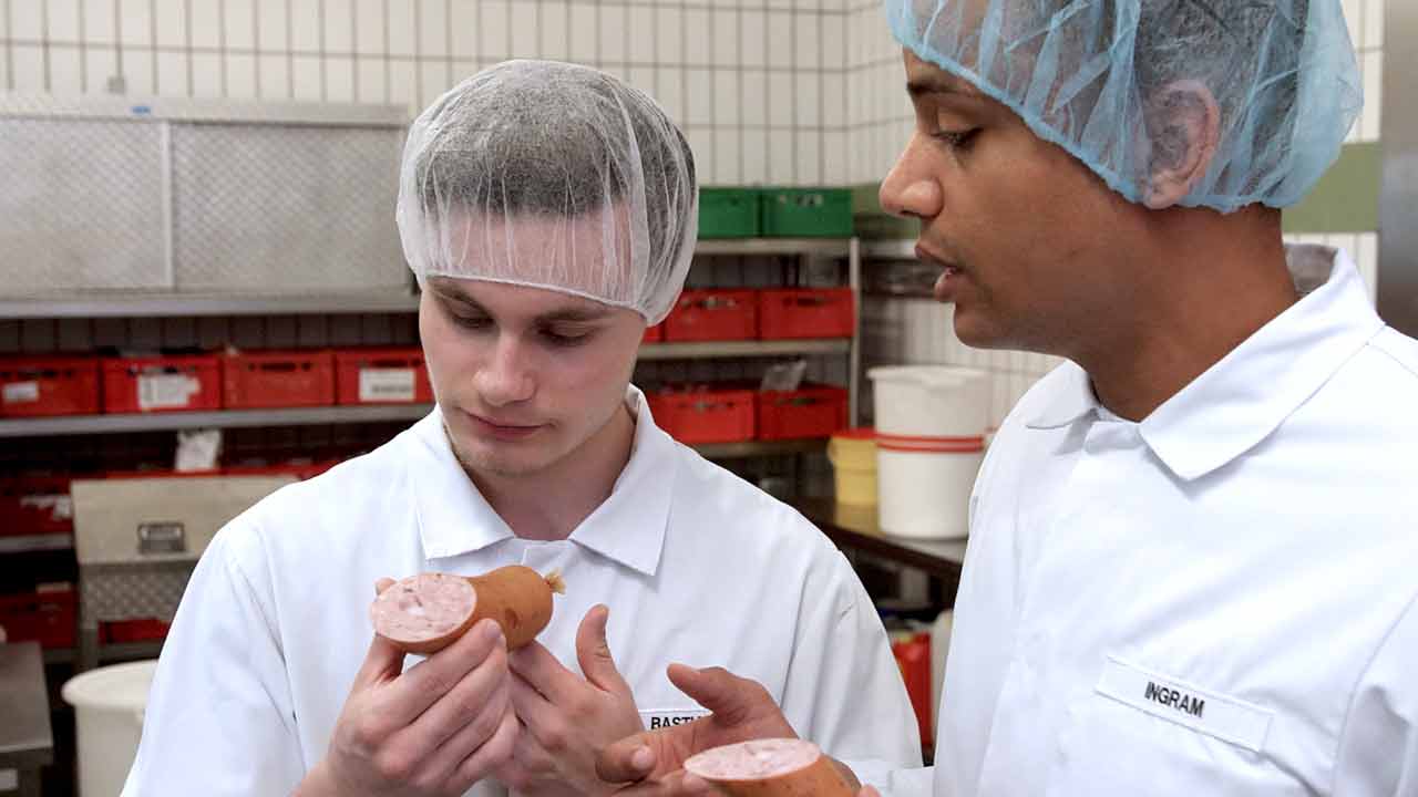 Ein Auszubildender vom Wurst-Basar begutachtet mit dem Ausbildungsleiter die Qualität einer Wurst. Recruitingvideo-Produktion Hannover von 52° Film.